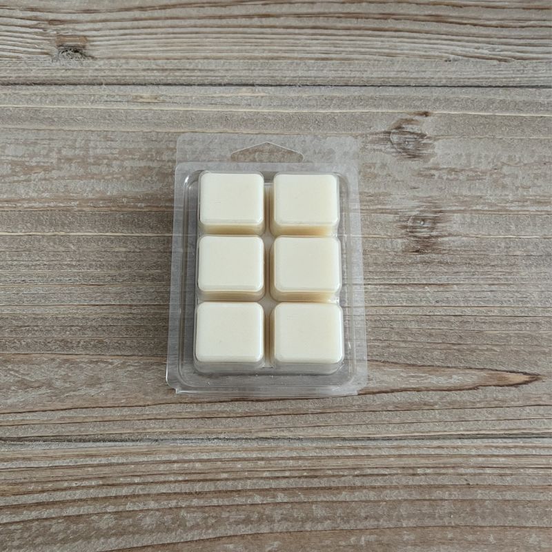 Χειροποίητα wax melts από φυσικό κερί σόγιας και καρύδας σε λευκό χρώμα, 6 αρωματικοί κύβοι σε διάφανη συσκευασία επάνω σε ξύλινη επιφάνεια.